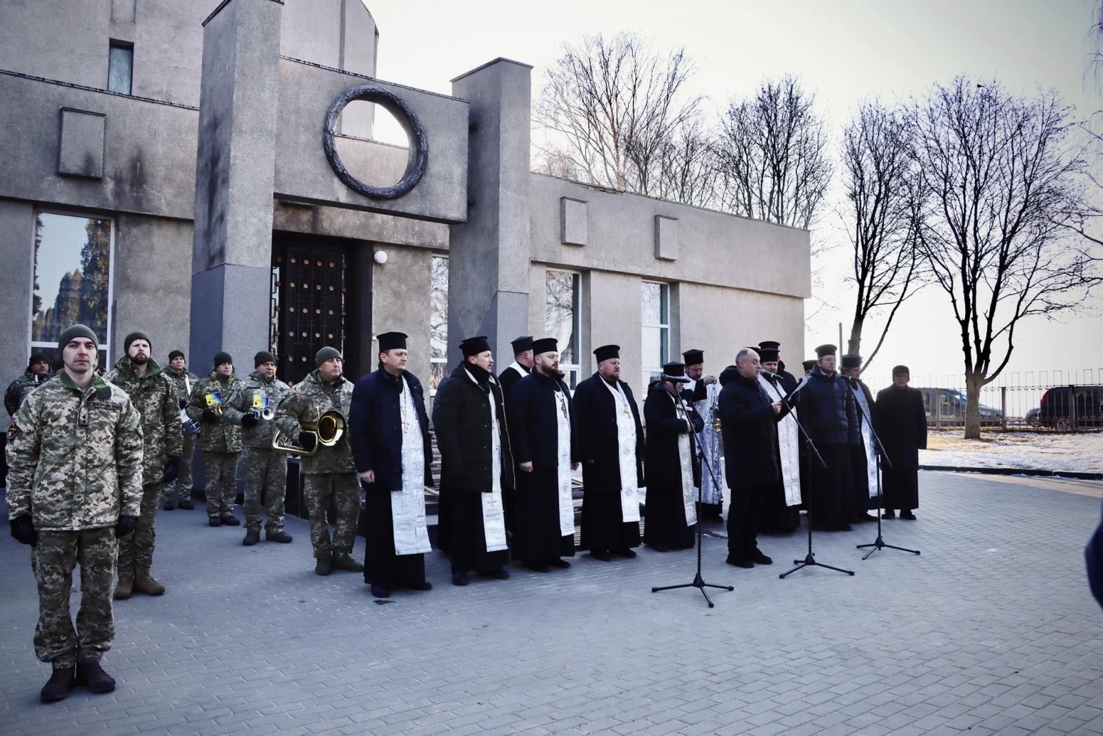 Чоловік виголошує промову. На задньому фоні стоять священники та військові.